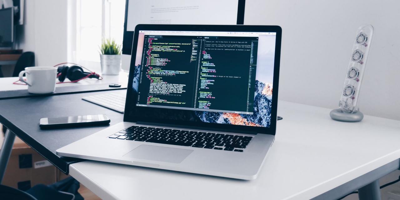 A MacBook with lines of code on its screen on a busy desk